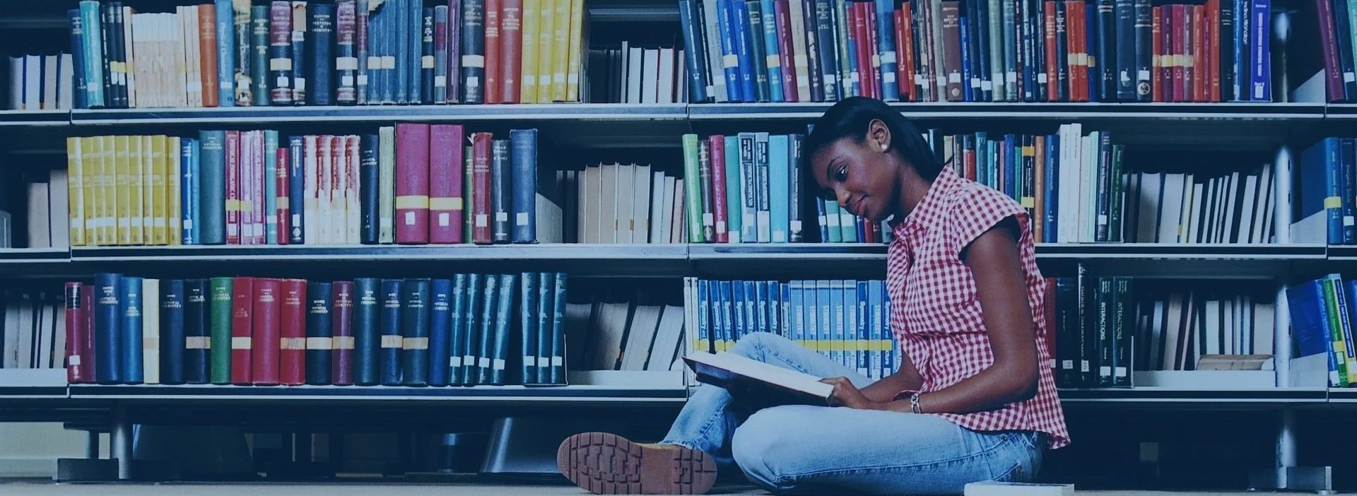 A girl sitting on the floor reading in front of some books