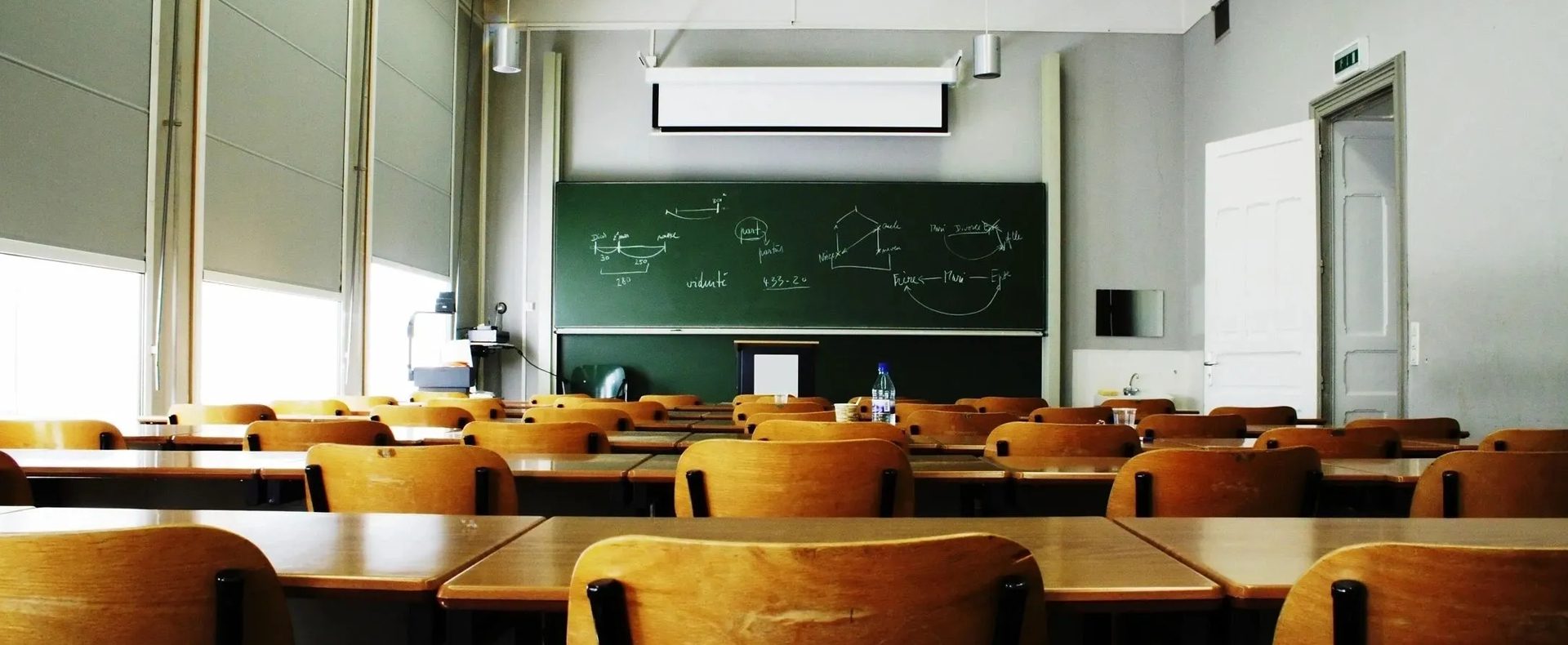 A classroom with desks and chairs in front of a chalkboard.